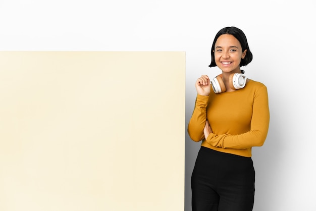 Junge Frau hört Musik mit einem großen leeren Plakat über isoliertem Hintergrund lachen