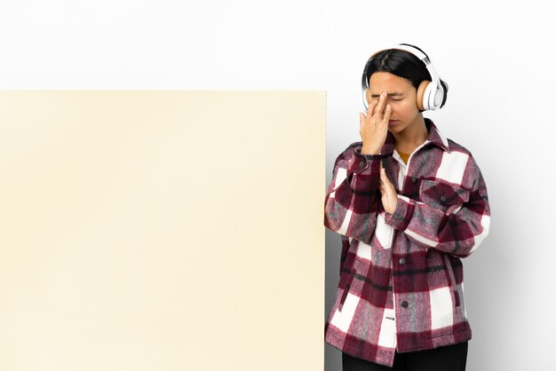 Junge Frau hört Musik mit einem großen leeren Plakat über isoliertem Hintergrund mit Kopfschmerzen