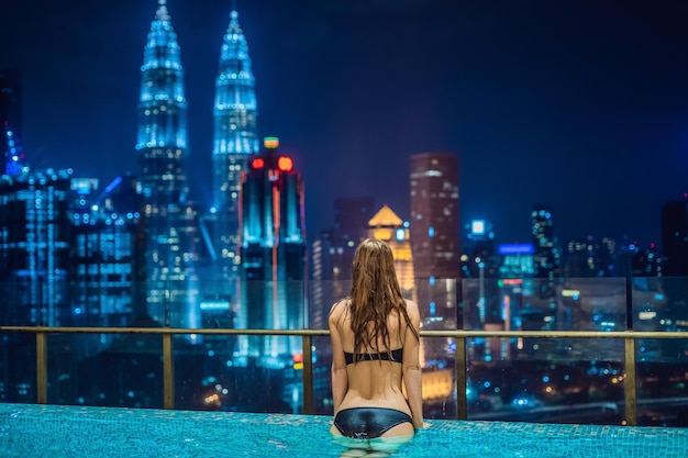 Junge Frau im Außenpool mit Blick auf die Stadt bei Nacht