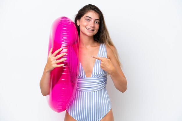 Junge Frau im Badeanzug, die einen Luftmatratz-Donut auf weißem Hintergrund hält und darauf hinweist