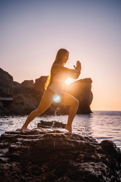 Junge Frau im Badeanzug mit langen Haaren, die sich an einem sonnigen Tag im Freien auf einer Yogamatte am Meer ausdehnt Frauen-Yoga-Fitness-Pilates-Routine Gesunder Lebensstil, Harmonie und Meditationskonzept