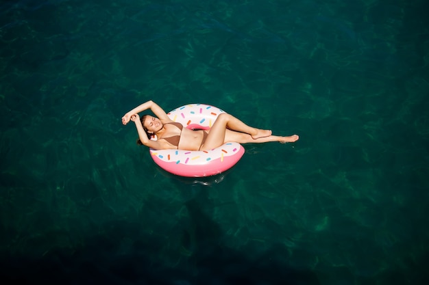 Junge Frau im Badeanzug schwimmt auf einem aufblasbaren Ring im Meer. Sommerferienkonzept.