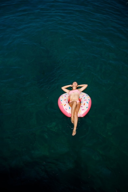 Junge Frau im Badeanzug schwimmt auf einem aufblasbaren Ring im Meer. Sommerferienkonzept.