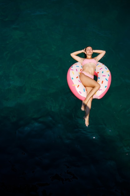 Junge Frau im Badeanzug schwimmt auf einem aufblasbaren Ring im Meer. Sommerferienkonzept.