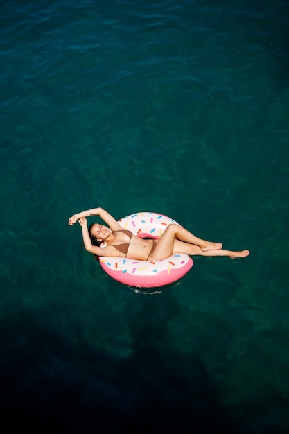 Junge Frau im Badeanzug schwimmt auf einem aufblasbaren Ring im Meer. Sommerferienkonzept.