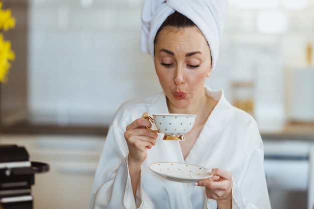 Junge Frau im Bademantel trinkt einen Morgenkaffee in der heimischen Küche.