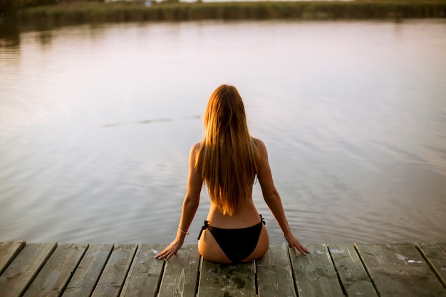 Junge Frau im Bikini, der auf einem Pier am See sitzt