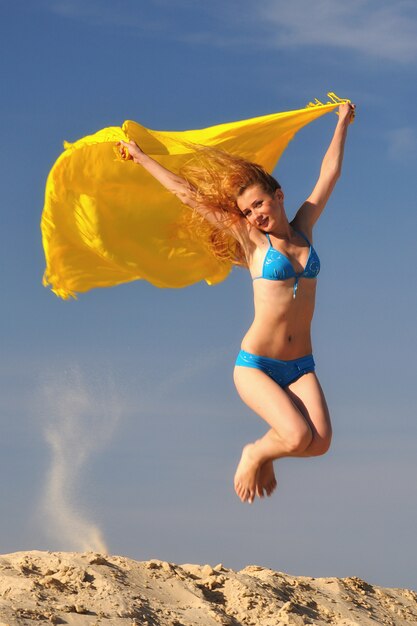 Junge Frau im Bikini, der über Sand mit Regenschirm in Händen springt