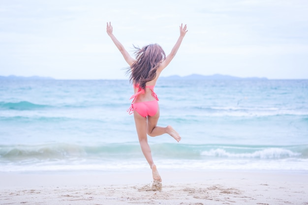 Junge Frau im Bikini springend auf den Sandstrand und Wellen und entspannend, Sommerreisekonzept.