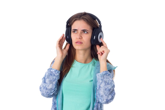 Junge Frau im blauen Hemd, die Musik in schwarzen Kopfhörern auf weißem Hintergrund im Studio hört