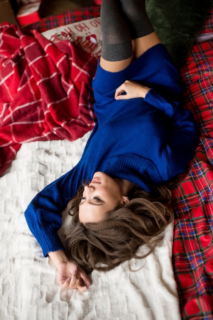 Junge Frau im blauen Kleid liegt auf dem Bett, Weihnachtsdekor