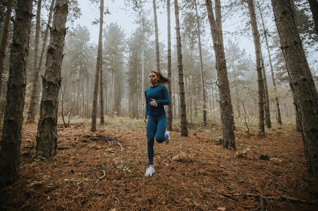 Junge Frau im blauen Trainingsanzug, die im Herbst auf dem Waldweg in Richtung Kamera läuft