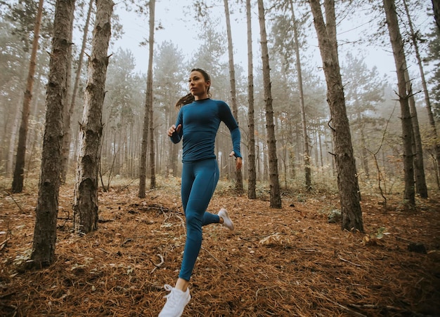 Junge Frau im blauen Trainingsanzug, die im Herbst auf dem Waldweg in Richtung Kamera läuft