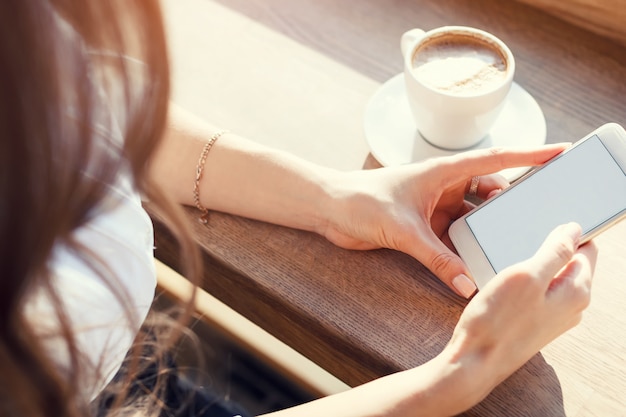 Junge Frau im Café benutzt Handy und trinkt Kaffee