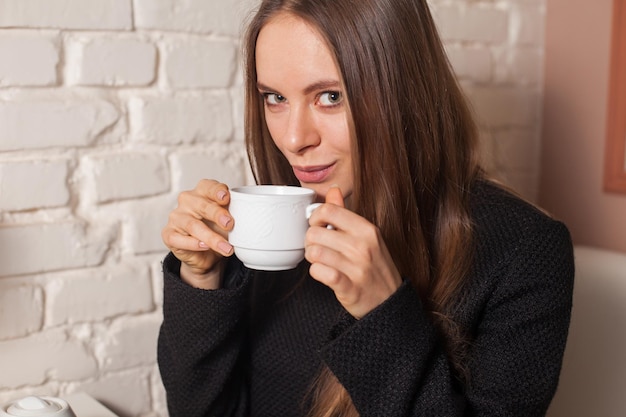 Junge Frau im Café, die hier Lieblingsgetränktee in weißer Tasse trinkt