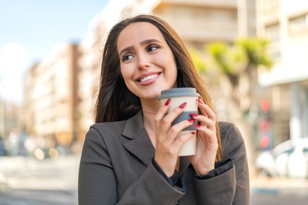 Junge Frau im Freien hält einen Kaffee zum Mitnehmen in der Hand und hat Zweifel