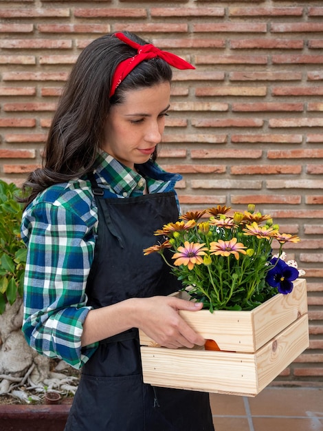 Junge Frau im Garten zu Hause mit Blumentopf in Holzkiste