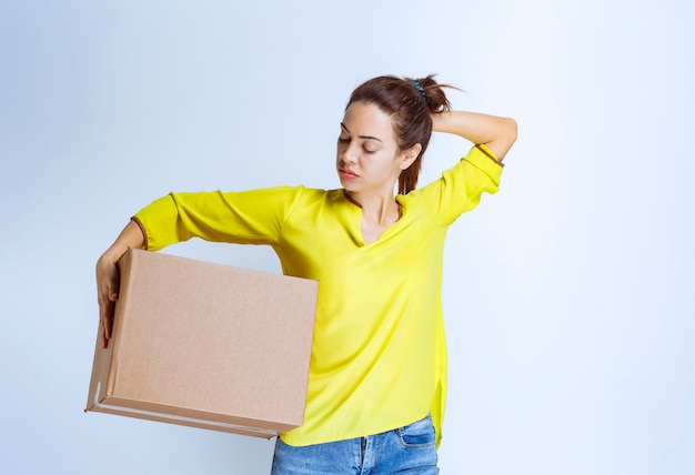 Junge Frau im gelben Hemd, die ein Papppaket hält und nachdenklich schaut