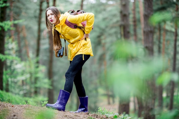 Junge Frau im gelben Regenmantel, die während der Reise im Wald Probleme mit Knieschmerzen hat