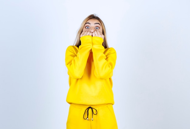 Junge Frau im gelben Trainingsanzug bedeckt ihren Mund über der weißen Wand