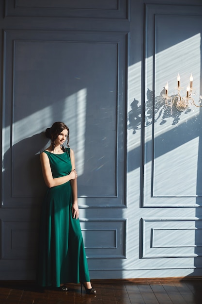 Junge Frau im grünen Abendkleid steht nahe der blauen Wand im Weinleseinnenraum.