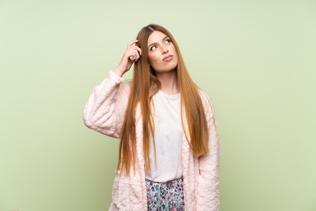 Junge Frau im Hausmantel über der grünen Wand, die Zweifel hat und mit verwirren Gesichtsausdruck