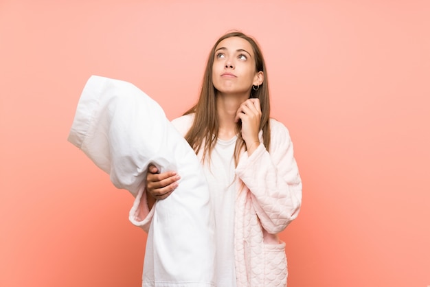 Junge Frau im Hausmantel über der rosa Wand eine Idee denkend