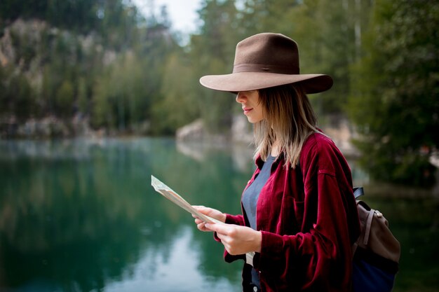 Junge Frau im Hut und im roten Hemd mit Karte nahe See