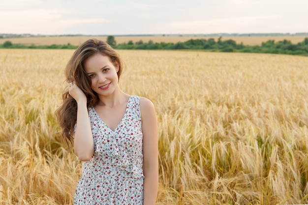 Junge Frau im Kleid auf Sommerweizenfeld. Lächelndes Mädchen auf goldener Wiese. Freiheit