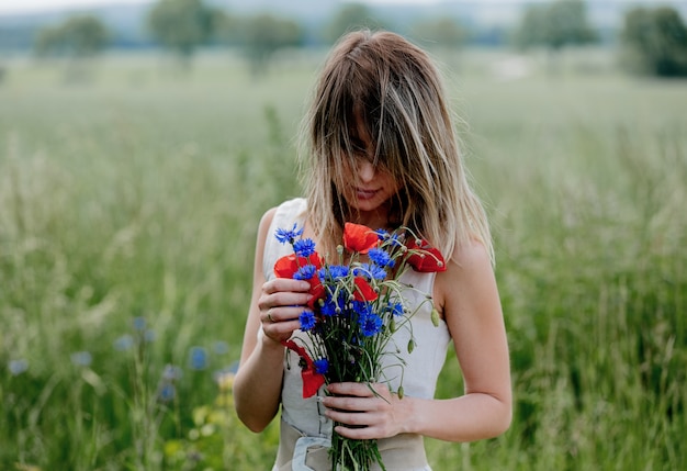 Junge Frau im Kleid bleiben in der Nähe des Feldes mit Blumenstrauß von Centaurea und Mohnblumen