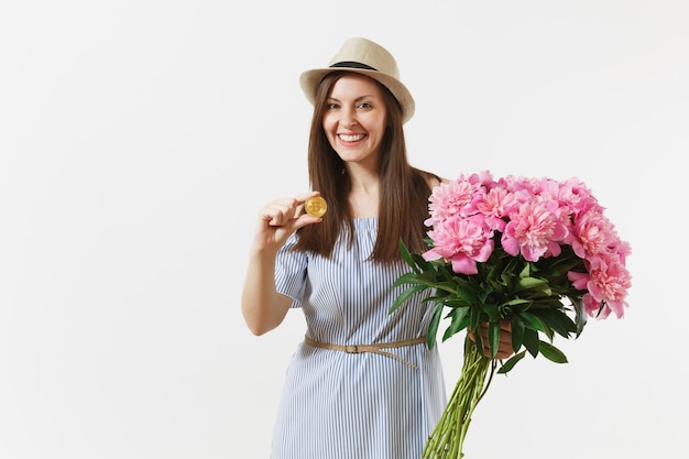 Junge Frau im Kleid, Hut, der Bitcoin hält, Münze der goldenen Farbe, Blumenstrauß der schönen rosa Pfingstrosenblumen lokalisiert auf weißem Hintergrund. Geschäft, Lieferung, Online-Shopping, virtuelles Währungskonzept.