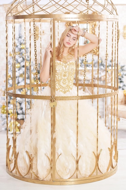 Junge Frau im Kleid posiert im goldenen Käfig im Zimmer, das für die Weihnachtsferien dekoriert ist