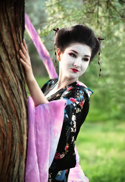 Junge Frau im Kostüm der Geisha, die nahe Baum steht