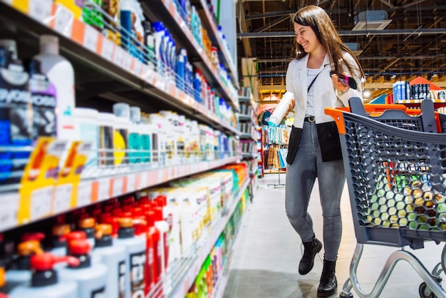 Junge Frau im Laden mit Einkaufswagen wählt Shampoo im Supermarkt-Einkaufskonzept-Kopienraum