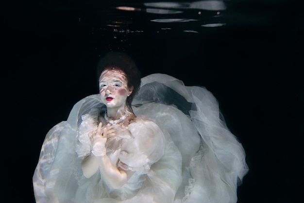 junge Frau im langen weißen Luxuskleid unter Wasser auf dem schwarzen Hintergrund. Bewegung, Kunst, Winter