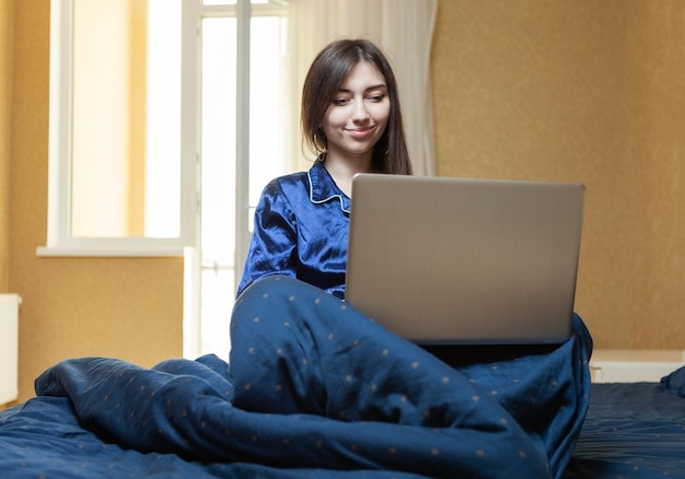 Junge Frau im Nachthemd sitzt im Bett und benutzt Laptop