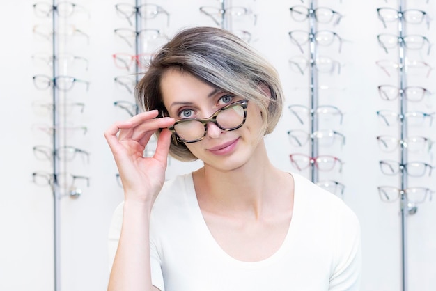 Junge Frau im Optikgeschäft wählt neue Brille mit Optikerbrille im Optikgeschäft Eine Frau wählt eine Brille Emotionen Augenheilkunde