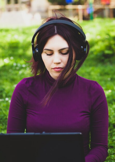 Junge Frau im Park unter Verwendung der hörenden Musik der Laptop-Computers.