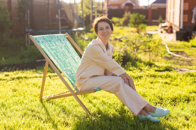 Junge Frau im Pyjama ruht im Stuhl auf einem grünen Rasen am sonnigen Sommertag Dorf- und Landleben