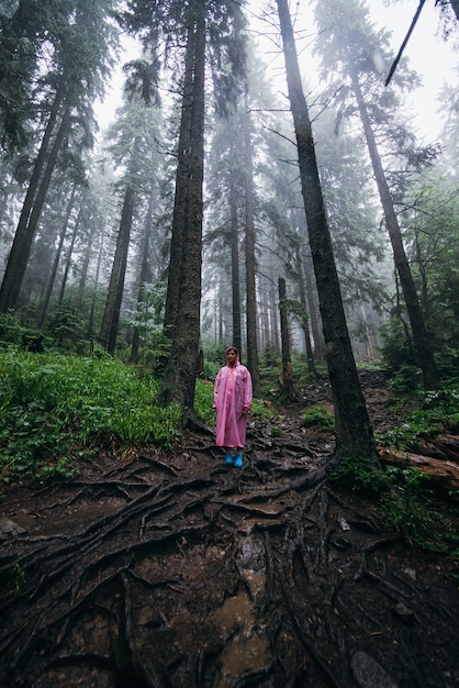Junge Frau im Regenmantel geht im Regen durch den Wald