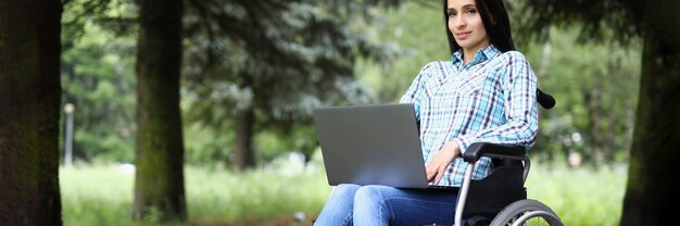 Junge Frau im Rollstuhl arbeitet am Laptop im Park