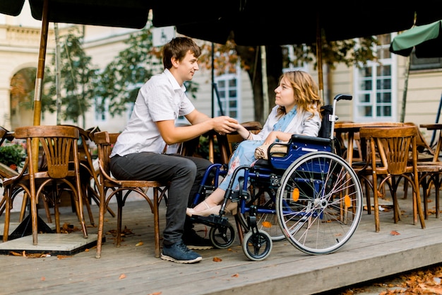 junge Frau im Rollstuhl genießt eine gute Gesellschaft bei einem Date mit ihrem gutaussehenden Mann in einem Café im Freien in der Stadt