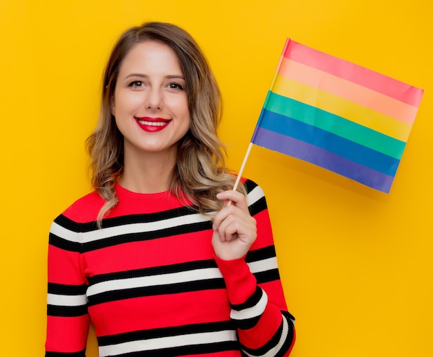 Junge Frau im rot gestreiften Pullover mit LGBT-Flagge auf Gelb