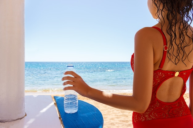 Junge frau im roten badeanzug am strand hält eine wasserflasche