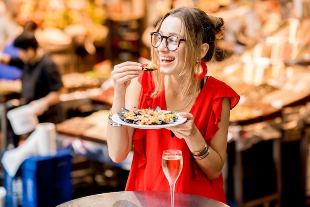 Junge Frau im roten Kleid beim Mittagessen mit Muscheln und Roséwein auf dem Lebensmittelmarkt?