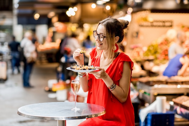 Junge Frau im roten Kleid beim Mittagessen mit Muscheln und Roséwein auf dem Lebensmittelmarkt?