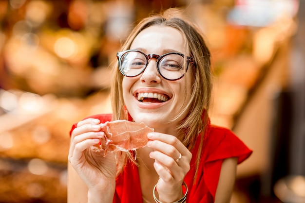 Junge Frau im roten Kleid isst Jamon traditionellen spanischen Trockenschinken, der auf dem Lebensmittelmarkt von Barcelona sitzt?