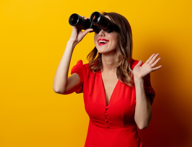 Junge Frau im roten Kleid mit Binokel auf gelber Wand