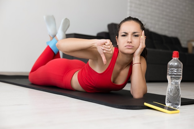 Junge Frau im roten Trainingsanzug, der Übung oder Yoga zu Hause tut