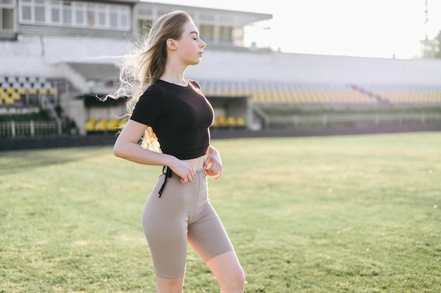 Junge Frau im schwarzen Oberteil, die Fahrräder anpasst Mädchen steht seitlich vor dem Hintergrund des Sportplatzes